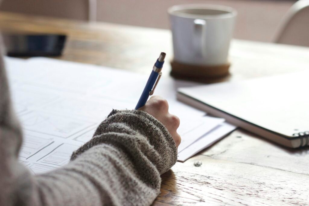 person writing on brown wooden table near white ceramic mug person writing on brown wooden table near white ceramic mug